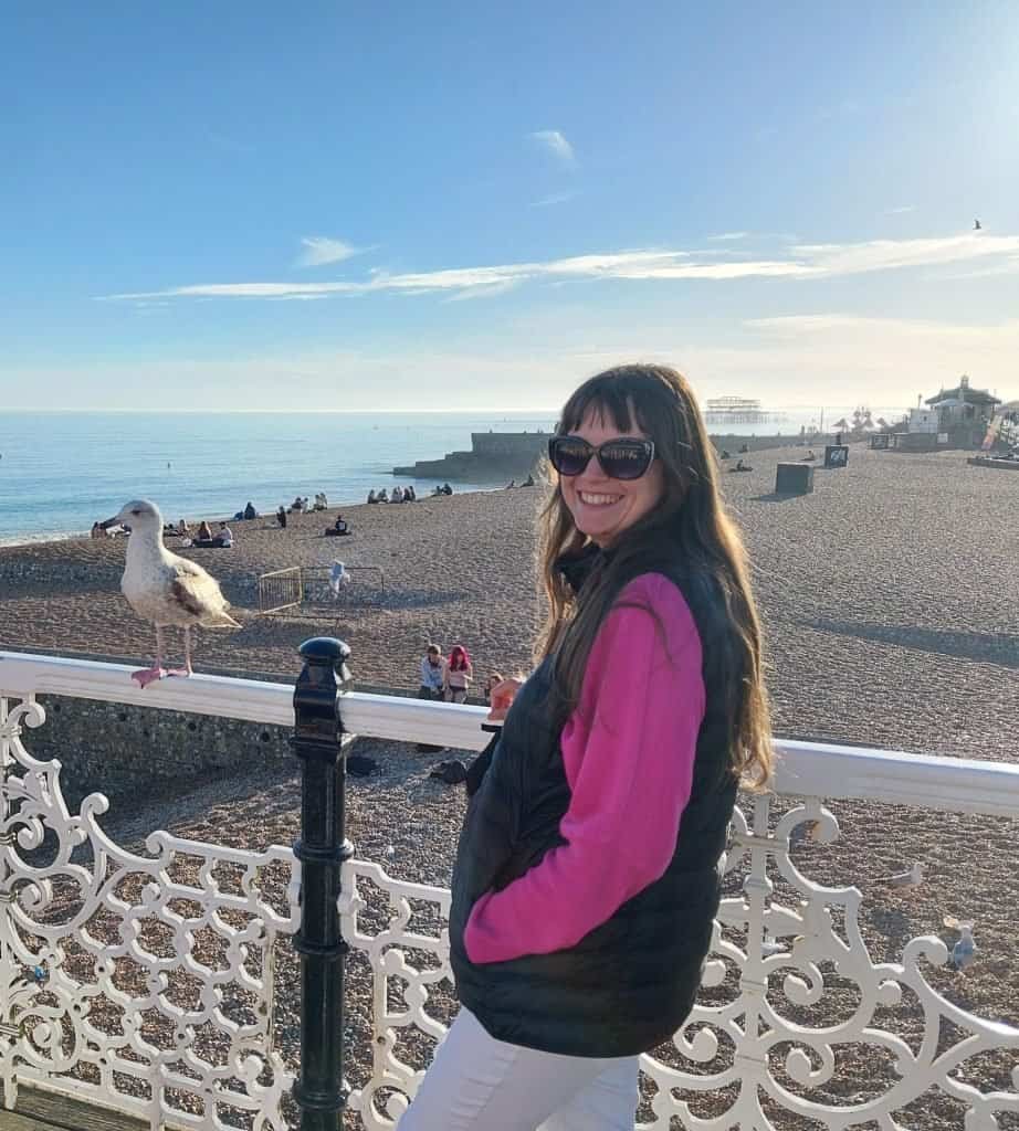 Dr. Nataliia Reva smiling on the Brighton seafront, with the beach, sea and West Pier behind her — portrait